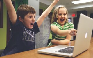 A boy and girl sitting at a laptop celebrating a win on screen