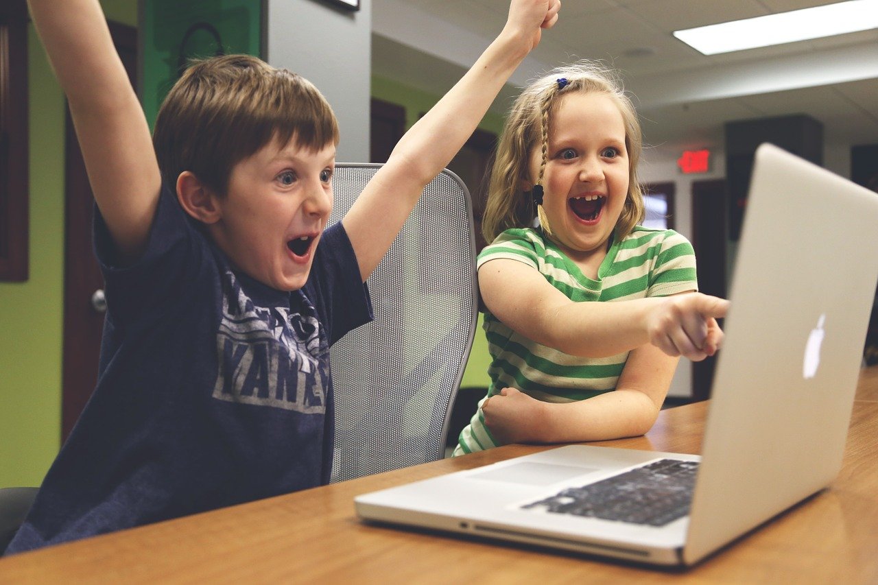 A boy and girl sitting at a laptop celebrating a win on screen
