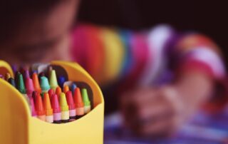 Colourful crayons in a pot with a child drawing behind