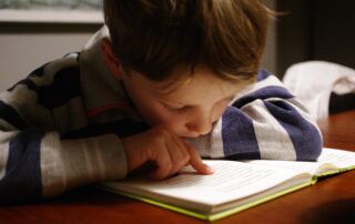 Small boy leaning over a book and reading