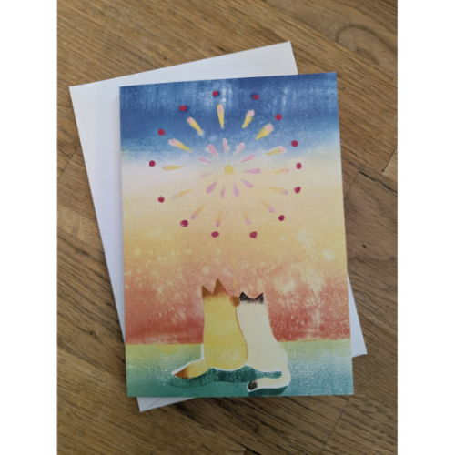 A yellow cat and a white cat looking up at a firework